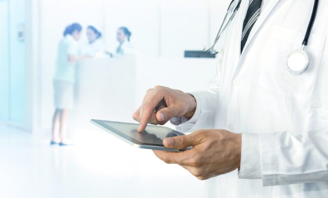 Concept of hospital automation management technology and Internet of Things for smart health care with paperless technology. Doctor with stethoscope using a tablet to check patient status.